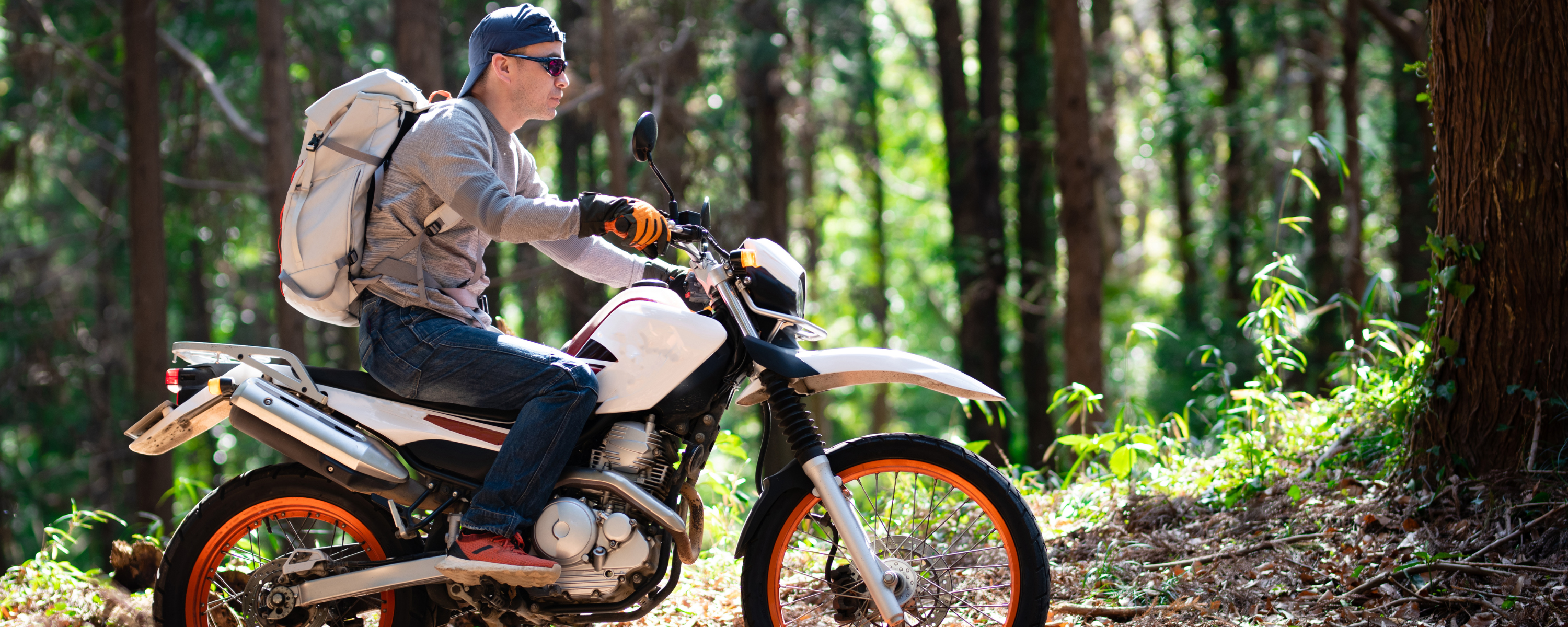 A man wearing motor Sunglasses and riding his motorcycle in forest.